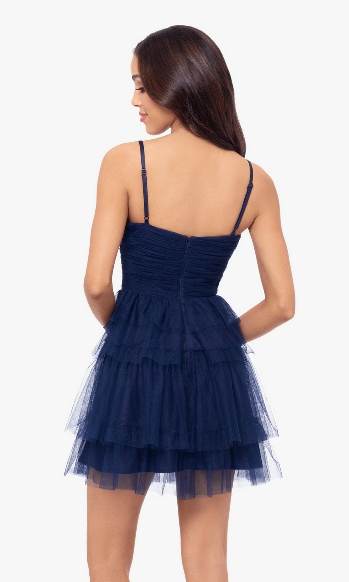 A woman stands facing away, wearing the Cut-Out Short Ruffled Homecoming Dress 5098BN: a navy blue sleeveless A-line dress with spaghetti straps and a fitted ruched sweetheart bodice.